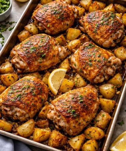 Juicy, crispy lemon garlic chicken thighs with roasted potatoes on a baking sheet.